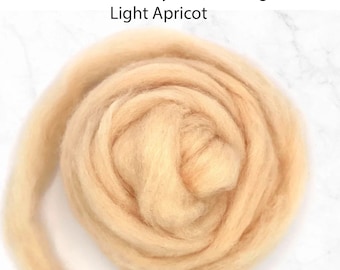 May include: A close-up of a light apricot Corriedale bulky wool roving. The wool is soft and fluffy, and it is perfect for spinning or felting.