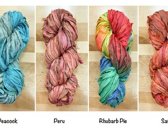 Könnte beinhalten: Vier Knäuel Seidenbandgarn in verschiedenen Farben: Pfauenblau, peruanisches Rosa, Rhabarberkuchen und Safran. Das Garn besteht aus recycelter Seide und ist perfekt zum Stricken, Häkeln und Weben.