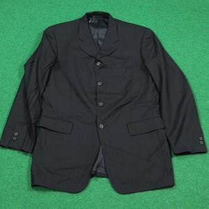 以下が含まれることがあります： ノッチドラペル、4つボタン留め、2つのフロントポケットが付いた黒いブレザー。 ブレザーはテクスチャード加工された生地で作られており、袖にボタンが付いています。 衣類は緑色の表面に表示されています。