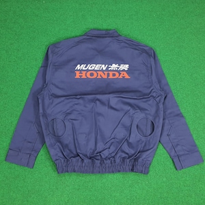 Puede incluir: Una chaqueta azul marino de manga larga con el texto MUGEN y HONDA impreso en blanco y naranja en la espalda. La chaqueta incluye un cuello, una cintura elástica fruncida y dos aberturas circulares en la parte inferior de la espalda.