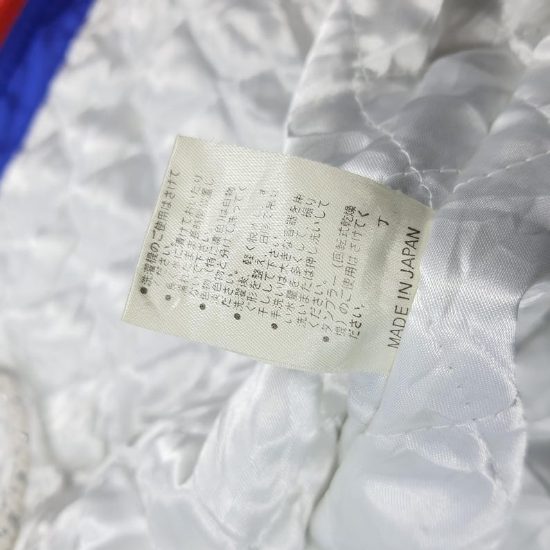 May include: Close-up of a white quilted fabric with a tag attached. The tag has Japanese text and the words "MADE IN JAPAN". The fabric appears to be part of a garment's lining.