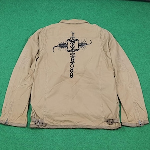 May include: Tan jacket with a black graphic design on the back. The jacket has a button-down front, pockets, and adjustable straps at the waist. The graphic appears to be a stylized insect or creature with Japanese characters.
