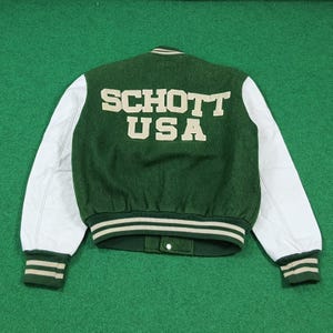 May include: Green and white varsity jacket with the text "SCHOTT USA" on the back. The jacket has white leather sleeves, a green wool body, and green and white striped cuffs and hem.