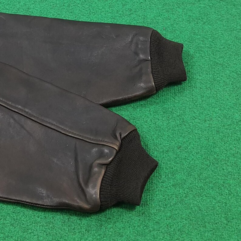 Puede incluir: Un par de mangas de chaqueta de cuero marr&oacute;n oscuro con pu&ntilde;os de punto acanalado negro en los extremos. Las mangas est&aacute;n construidas con costuras visibles a lo largo del cuero, mostrando una textura suave y un dise&ntilde;o estructurado.