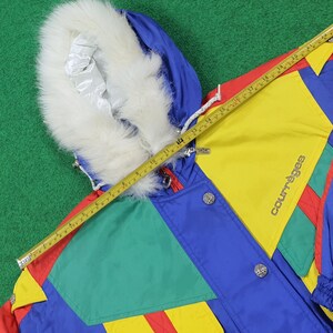 May include: A colorful vintage jacket with a fur-lined hood. The jacket features a patchwork design in red, blue, yellow, and green. The brand name "Courr&egrave;ges" is visible on the jacket. A measuring tape is laid across the jacket.