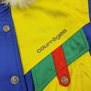 May include: A colorful jacket with a blue, yellow, green, and red design. The jacket features the brand name "Courr&egrave;ges" in silver lettering. Silver buttons and a white fur collar add detail to the garment.