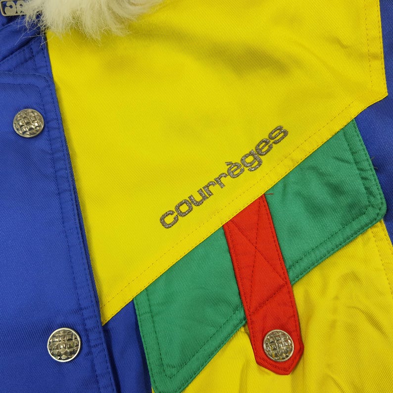 May include: A colorful jacket with a blue, yellow, green, and red design. The jacket features the brand name "Courr&egrave;ges" in silver lettering. Silver buttons and a white fur collar add detail to the garment.