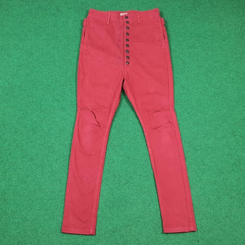May include: Red denim pants with a button-up fly. The pants have a high waist and a slim fit. The knees have a distressed look. The pants are made of a sturdy denim material.