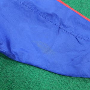 May include: Close-up of a blue fabric with a red stripe along the edge. The fabric has a visible seam and a stain. The background is green.