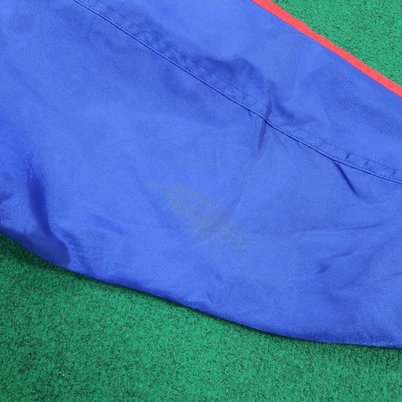 May include: Close-up of a blue fabric with a red stripe along the edge. The fabric has a visible seam and a stain. The background is green.