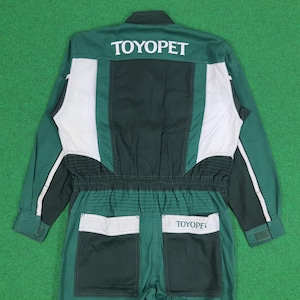 May include: A long-sleeve jumpsuit in dark green, forest green, and white. The back features the text TOYOPET in white lettering across the shoulders and on the right back pocket. It includes a gathered elastic waist and two back pockets.