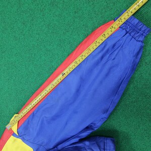 May include: A colorful garment with red, blue, and yellow panels. A yellow and red measuring tape is laid across the garment, showing measurements in inches. The garment is on a green surface.