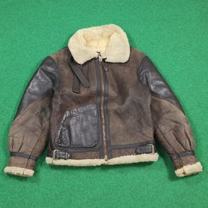 Puede incluir: Chaqueta de cuero marr&oacute;n con cuello y ribetes de borreguillo color crema. La chaqueta tiene cremallera frontal, bolsillo en el pecho y detalles de hebillas en la cintura y los pu&ntilde;os. Las mangas son de color marr&oacute;n oscuro.