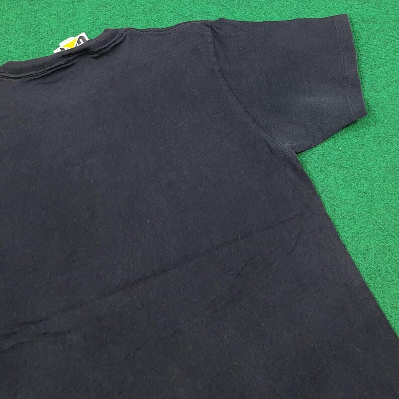 May include: A solid black short-sleeved t-shirt featuring a crew neckline and a small white and yellow brand tag attached to the inside of the collar. The garment is plain with no additional graphics or patterns visible on the fabric surface.