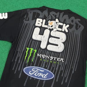 May include: A black short-sleeve t-shirt featuring a large graphic print on the back. The design includes the text BLOCK 43 with a skull icon, a green Monster Energy logo, and a blue Ford oval logo, all set against a grey dripping paint effect.