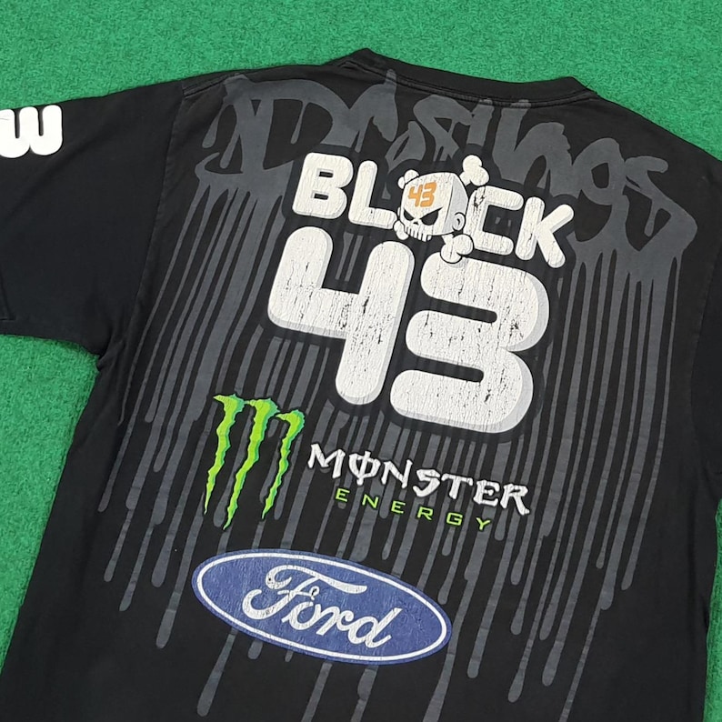 May include: A black short-sleeve t-shirt featuring a large graphic print on the back. The design includes the text BLOCK 43 with a skull icon, a green Monster Energy logo, and a blue Ford oval logo, all set against a grey dripping paint effect.