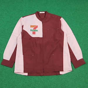 Puede incluir: Una camisa de trabajo de manga larga con un diseño de bloques de color. La camisa es principalmente granate y rosa claro, con el logo "7-Eleven" en el pecho. Tiene cuello mandarín, cierre de cremallera y dos bolsillos delanteros. Las mangas tienen un bloque de color contrastante.
