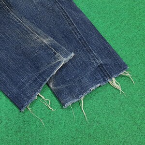 K&ouml;nnte beinhalten: Nahaufnahme des ausgefransten Saums einer blauen Jeans. Die Jeans hat einen Used-Look mit sichtbaren Abnutzungserscheinungen. Die Kanten sind unfertig, mit losen F&auml;den. Der Hintergrund ist einfarbig gr&uuml;n.