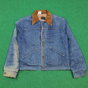 Puede incluir: Chaqueta vaquera azul con cuello de pana marrón y forro color crema. La chaqueta tiene dos bolsillos delanteros y cierre de botones. La marca "Wrangler" es visible en el cuello.
