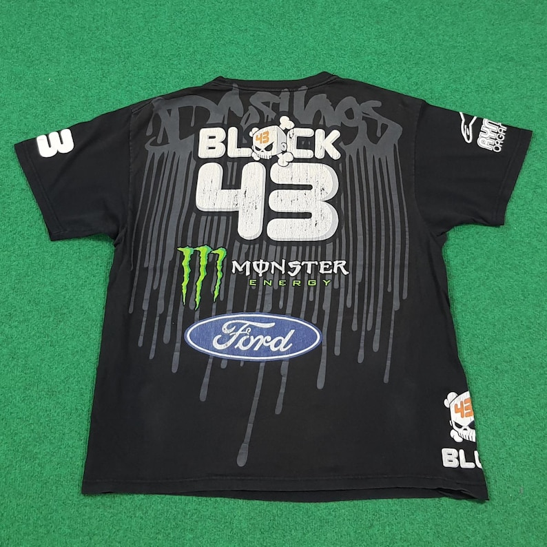 May include: A black short-sleeve t-shirt featuring a large graphic print with the text BLOCK 43, a skull icon, a Monster Energy logo, and a Ford logo. The design includes grey paint drip effects, the number 3 on the sleeve, and additional branding.
