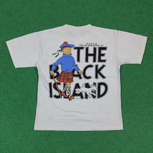 May include: White t-shirt featuring a cartoon illustration from "The Adventures of The Black Island." The design includes a character in a blue sweater and kilt, a dog, and the title text in black. The shirt has short sleeves.