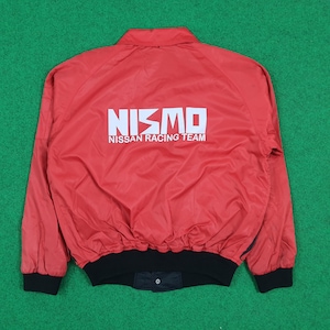 May include: Red nylon jacket featuring the white text "NISMO NISSAN RACING TEAM" on the back. The jacket has a black ribbed hem and cuffs. The jacket is a size medium.