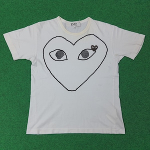 Può includere: T-shirt bianca con un grande cuore nero con occhi. La maglietta ha maniche corte e girocollo. La parola "PLAY" è stampata sulla parte superiore del petto. La maglietta è realizzata in un materiale morbido e confortevole.