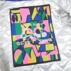 May include: A rectangular label with a colorful abstract design. The design features geometric shapes in pink, green, blue, yellow, and orange against a black background. The text "esprit futur" and "courreges" are visible.
