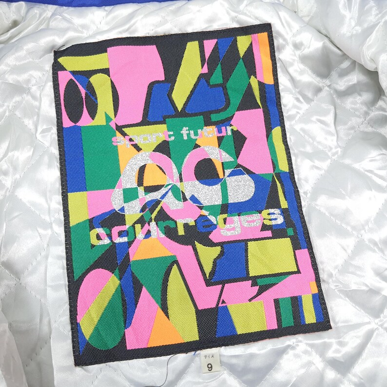 May include: A rectangular label with a colorful abstract design. The design features geometric shapes in pink, green, blue, yellow, and orange against a black background. The text "esprit futur" and "courreges" are visible.