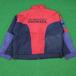 Może przedstawiać: Czerwona, granatowa i fioletowa kurtka z napisem "MUGEN HONDA" z tyłu. Kurtka ma wysoki kołnierz i zapięcie na zamek błyskawiczny. Rękawy są fioletowe, a korpus czerwony i granatowy.