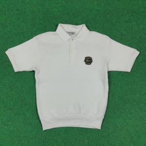 May include: A white short-sleeved polo shirt with a collar and a three-button placket. The shirt features a small emblem on the chest. The shirt is made of a soft, textured fabric and has a ribbed hem.