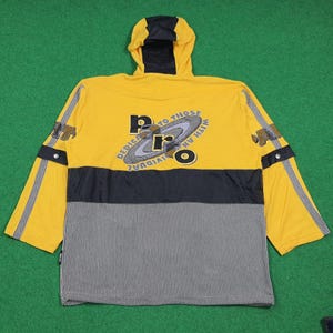 May include: Yellow hooded jacket with black and white striped lower section. The jacket features the text "PRO" in a circular design, with additional text. Black accents are on the hood, sleeves, and chest. The sleeves have a black and yellow stripe.