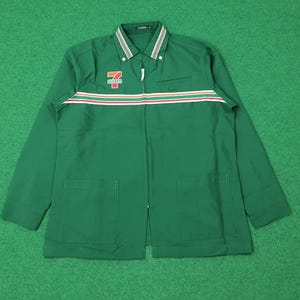 Puede incluir: Chaqueta verde de manga larga con cremallera completa y dos bolsillos delanteros. La chaqueta presenta una franja blanca, roja y naranja en el pecho y el logotipo de 7-Eleven en el pecho izquierdo. El cuello tiene un diseño a rayas.