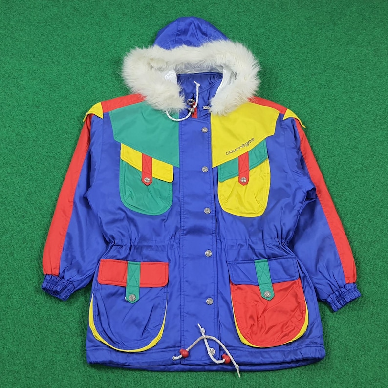 May include: A vibrant blue winter jacket with a fur-lined hood. The jacket features colorful accents of red, yellow, and green on the pockets and shoulders. The jacket has a drawstring waist and the brand name "courr&egrave;ges" is visible.