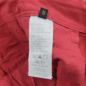 May include: Close-up of a red garment with a tag. The tag lists the fabric composition as 57% cotton, 40% tencel, and 3% polyurethane. Washing instructions are also printed on the tag. The tag also says "Made in Japan".
