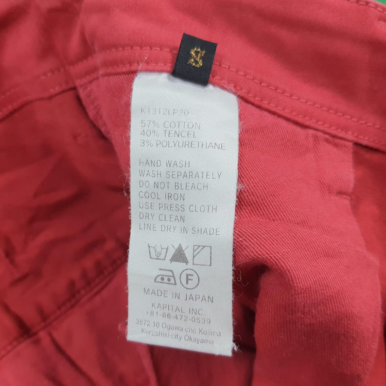 May include: Close-up of a red garment with a tag. The tag lists the fabric composition as 57% cotton, 40% tencel, and 3% polyurethane. Washing instructions are also printed on the tag. The tag also says "Made in Japan".