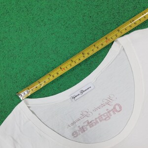 Puede incluir: Una camiseta blanca con cuello redondo y una etiqueta de marca que dice Hysteric Glamour. La camiseta presenta texto en rojo y negro que dice Hysteric Glamour Original Fake. Una cinta m&eacute;trica amarilla muestra un ancho de cuello de unos 28 cm.