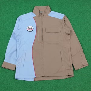 May include: A zip-up jacket featuring a color-blocked design in light blue and tan. The front includes a vertical curved seam with a thin pink accent line, a chest pocket with a flap, and a circular patch displaying a cartoon panda face graphic.
