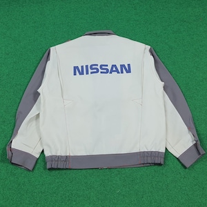 以下が含まれることがあります： 背中に青いブロック体で「NISSAN」の文字が入った白とグレーのジャケット。 ジャケットはグレーの袖とトリム、ボタンアップカラー、リブ編みの裾が特徴です。 ジャケットは緑色の表面に平らに置かれています。