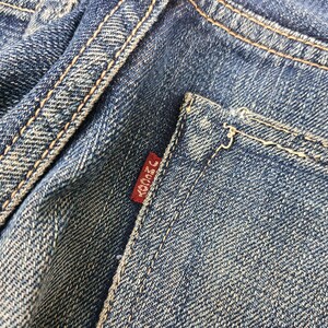 K&ouml;nnte beinhalten: Nahaufnahme von blauen Jeans mit sichtbaren N&auml;hten und einem kleinen roten Etikett. Das Etikett hat japanischen Text. Die Jeans weisen Gebrauchsspuren auf, mit Fokus auf dem Taschenbereich.