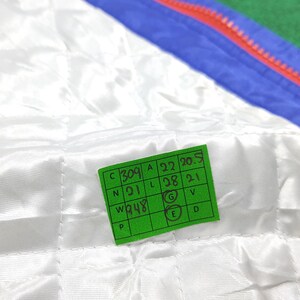 May include: Close-up of a white quilted fabric with a green tag. The tag has black text and numbers, including "309", "A 22 20.5", "N 21", "L 28 21", and "W 948". The fabric has a subtle sheen.