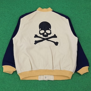 May include: Cream-colored bomber jacket with navy blue sleeves and a yellow collar and trim. The back features a large black skull and crossbones graphic. The jacket has a snap closure at the waist.