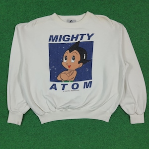 May include: White sweatshirt with a graphic of Astro Boy and the text "MIGHTY ATOM". The graphic is set against a blue starry background. The sweatshirt has long sleeves and a crew neck.