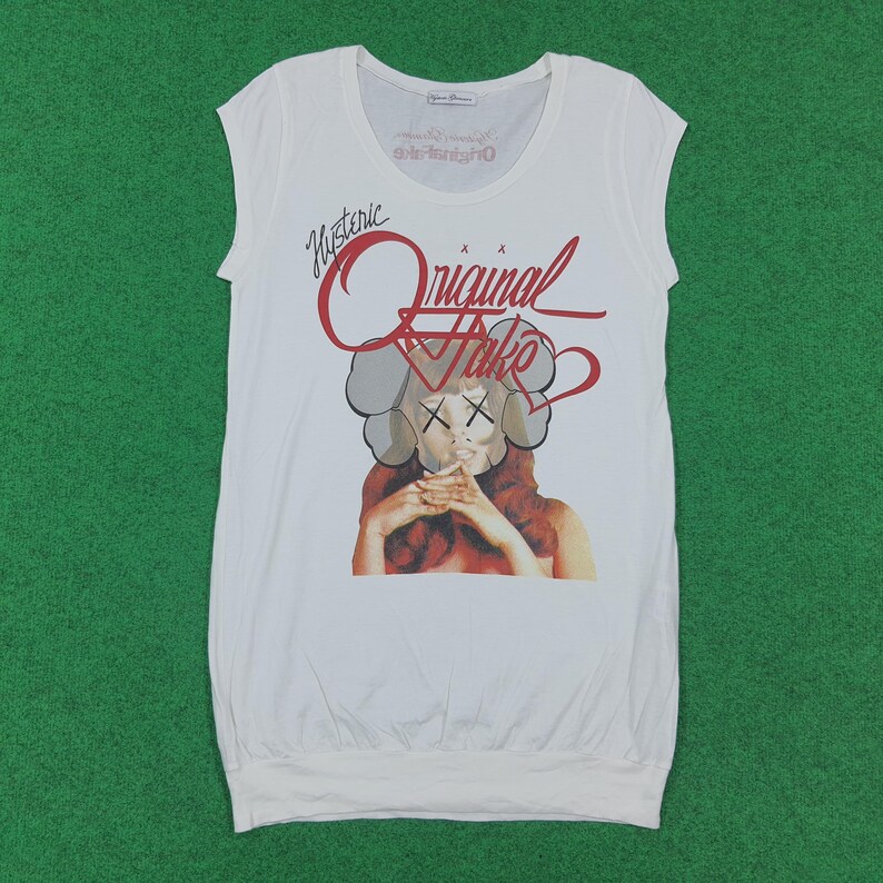 Puede incluir: Una camiseta blanca sin mangas con un estampado gr&aacute;fico de una persona con un tocado gris estilizado y ojos en forma de X. El texto rojo superior dice Hysteric Original Fake. El dise&ntilde;o incluye un contorno de coraz&oacute;n y un dobladillo redondeado.