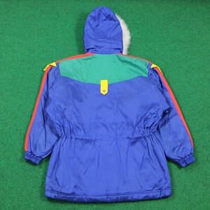 May include: A blue winter jacket with a hood and a white fur trim. The jacket has red and yellow accents on the shoulders and sleeves, with a green panel across the upper back. It features a drawstring waist and a yellow clasp.
