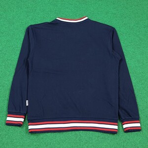 Puede incluir: Sudadera azul marino de manga larga con cuello redondo. El cuello y los pu&ntilde;os presentan rayas blancas y rojas. El logotipo de la marca es visible en el lado izquierdo. La sudadera es de material suave.