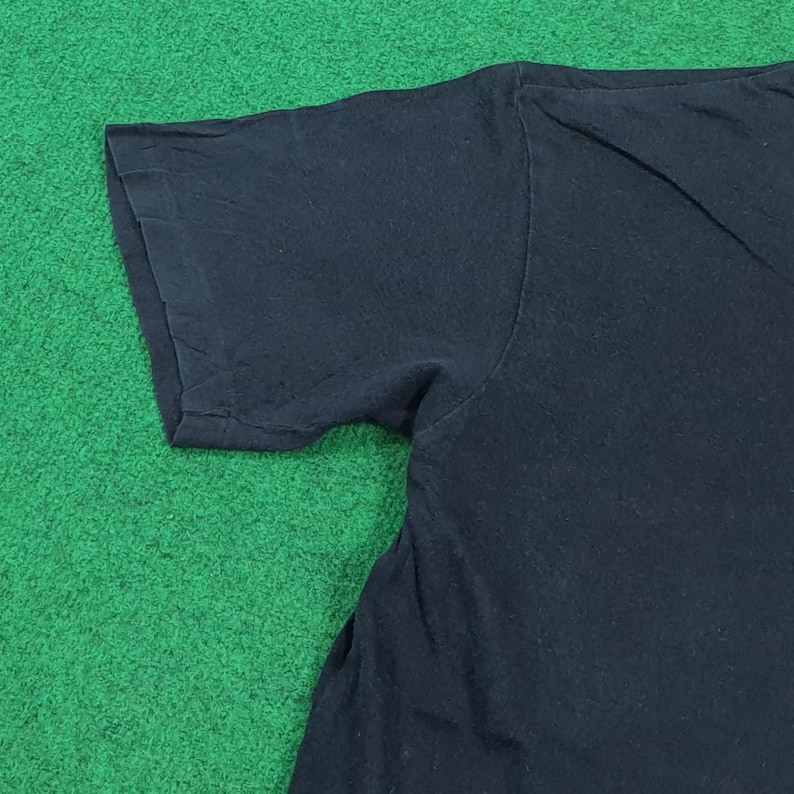 May include: A plain black short-sleeved t-shirt made of cotton fabric. The garment features a simple crew neckline and standard hemmed sleeves, showcasing a solid dark color throughout the visible portion of the shirt's upper torso and sleeve.