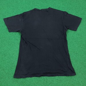 May include: A solid black short-sleeved t-shirt with a crew neckline. The garment is laid flat, displaying a plain, unadorned back side with a standard hemline at the sleeves and the bottom edge, constructed from a simple cotton-like fabric.