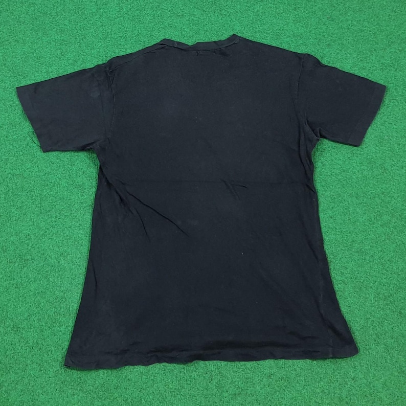 May include: A solid black short-sleeved t-shirt with a crew neckline. The garment is laid flat, displaying a plain, unadorned back side with a standard hemline at the sleeves and the bottom edge, constructed from a simple cotton-like fabric.
