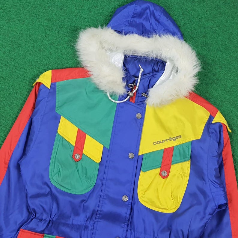May include: A vintage blue, red, green, and yellow winter jacket with a fur-lined hood. The jacket features the brand name "courr&egrave;ges" and has multiple pockets. The design includes color-blocked panels and a drawstring waist.